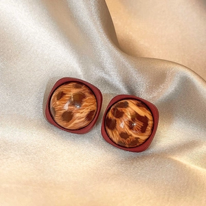 Macro detail of leopard print stud earrings on champagne silk fabric background