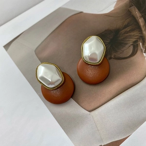 Detail of vintage round faux leather earrings with pearl and golden twisted frame