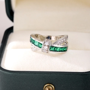 Macro shot of silver criss-cross ring with green emerald cut stones and white zircon