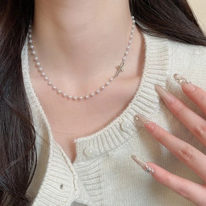 Close-up of pearl necklace with silver cross pendant worn on a minimalist knit cardigan