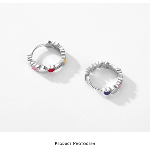 Macro detail of silver hoop earrings featuring colorful enamel heart patterns