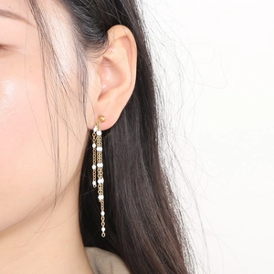 Detailed view of long gold tassel earrings with delicate white resin beads and chains