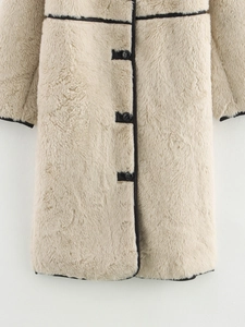Dettaglio del cappotto in ecopelliccia beige con bordi in pelle nera e bottoni scuri