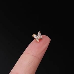 Macro shot of tiny gold butterfly ear stud with zircon stones on a fingertip