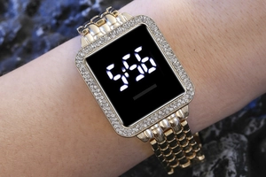 Close-up of gold LED digital watch with rhinestone bezel on a wrist showing 5:56