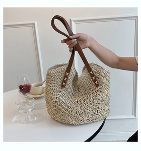 Detail of hand-woven straw bag with brown leather handles and decorative white cross-stitching