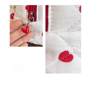 Detail of white quilted cosmetic bag featuring red heart prints and heart-shaped metal zipper