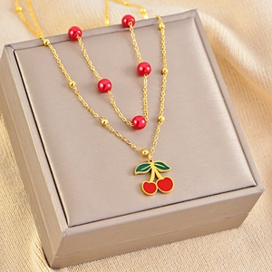 Close-up of golden cherry pendant necklace with red beads on a grey jewelry display box