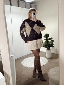 Detail of a brown argyle knit sweater paired with a beige pleated mini skirt and boots