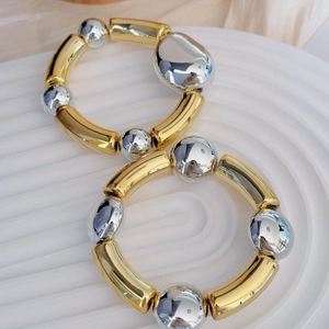 Minimalist two-tone elastic bracelet with gold metal tubes and silver beads on white surface