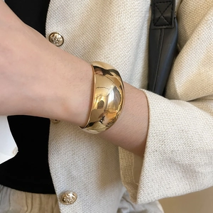 Gros plan d'un large bracelet manchette en métal doré poli sur le poignet d'un mannequin