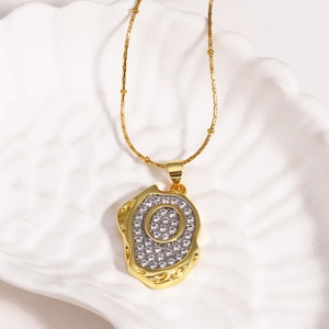 Macro view of gold plated 18k letter O pendant with cubic zirconia on a shell plate