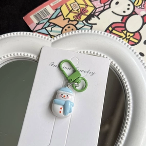 Detail shot of a cute snowman keychain with blue scarf and green clip on a display card