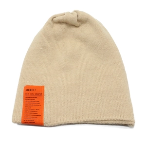 Detail of beige knit beanie featuring a vibrant orange MERCI fabric patch for winter