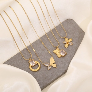 Four gold stainless steel necklaces with butterfly and geometric pendants on stone