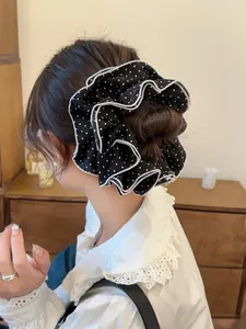 Detailed close-up of a black and white polka dot scrunchie with elegant white ruffled edges