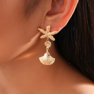 Close-up of golden starfish and shell drop earrings worn by a model for a beach style look