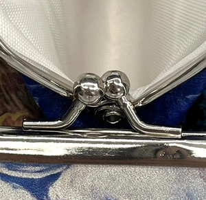 Detail of vintage kiss-lock metal clasp on floral print coin purse with blue fabric