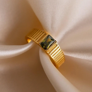 Golden birthstone ring with green emerald-cut stone on beige silk background