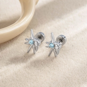 Silver starfish and seashell stud earrings with blue zircon on beige plush background