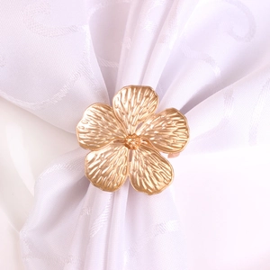 Matte gold five-petal flower napkin ring with intricate metal textures on white cloth