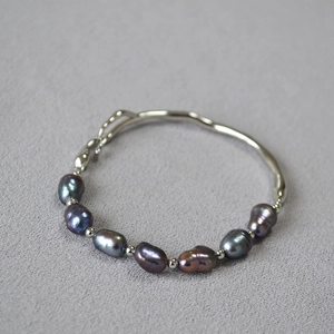 Detail of irregular baroque pearls and silver metal bar link bracelet on grey fabric