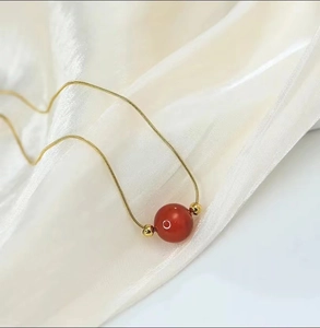 Elegant gold titanium steel necklace with a red agate bead and small gold charms