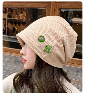 Detail view of a beige knit beanie with cute frog brooches worn by a model outdoors