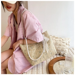 Detail of straw tote bag featuring floral embroidery, lace bow, and rope shoulder strap