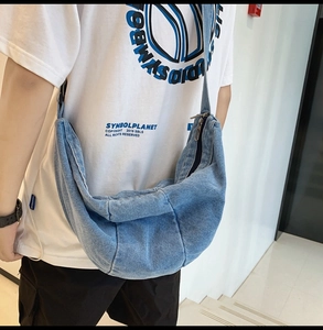 Detail of light blue washed denim crossbody bag showing moon-shaped texture and metal zipper