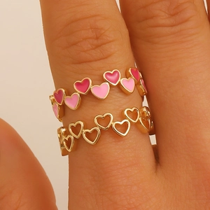 Dettaglio di cuori in smalto rosa e anelli a cuore dorati indossati su un dito