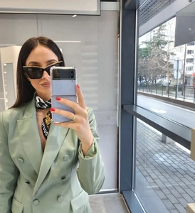 Close-up of black and gold frame cat eye sunglasses worn with a light green blazer