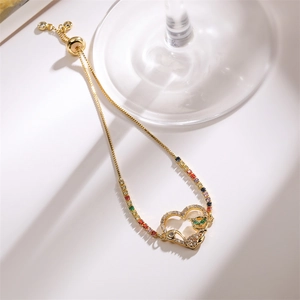 Détail d'un bracelet coeur doré avec motif chat et pierres de zircone arc-en-ciel colorées