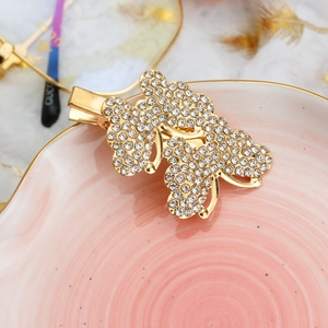 Elegant gold butterfly hair clip with crystals on a pink ceramic plate with white feathers