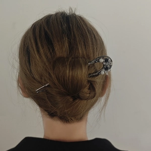 Detail of elegant silver U-shaped hair pin with floral motifs on a dark hair bun