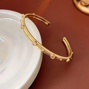 Detail of gold-plated spiral bangle with inlaid zircons leaning on a white ceramic plate