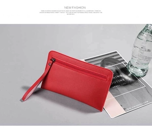 Detail of red leather zipper clutch bag with wristlet strap on a minimalist grey surface