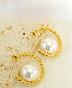 Detailed close-up of gold pearl hoop earrings on a textured stone and fabric background