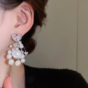 Dettaglio di orecchini con cuore in zircone e nappe di perle indossati da modella