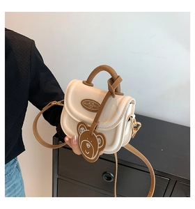 Detail of mini cream and brown crossbody bag with a cute bear charm and logo tag
