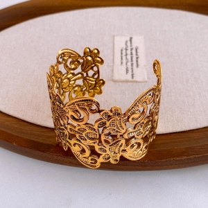 Detail of vintage gold open bangle with hollow floral patterns on a wooden tray