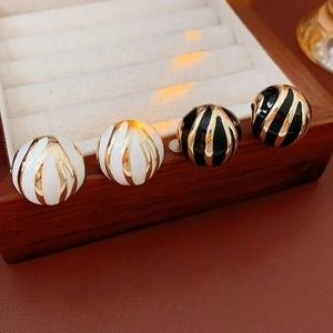 Close-up of black and white round enamel stud earrings with gold spiral texture details
