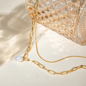 Detail of layered gold stainless steel necklace with round pearl pendant on glass