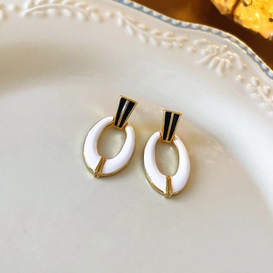 Detailed view of gold oval earrings with white enamel and black floral accents on a plate