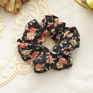 Close-up of floral fabric scrunchie with red rose patterns and purple dots on black fabric