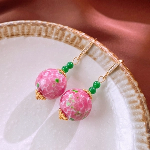 Orecchini pendenti vintage con perle di vetro rosa e ganci dorati su un vassoio ceramica
