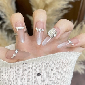 Macro shot of stiletto press-on nails with nude gradient, glitter, and luxury rhinestones