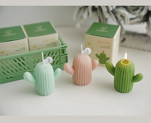 Gros plan de trois bougies cactus colorées dont une allumée près de boîtes cadeaux