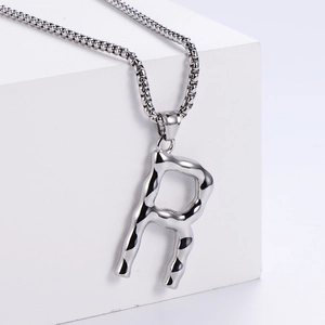 Détail macro du pendentif lettre R argenté avec texture lave sur une chaîne vénitienne
