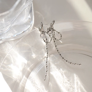 Detailed close-up of silver bow tassel earrings with white zircon on a glass edge
